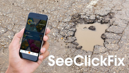 Hand holding cell phone taking picture of pot hole with words "SeeClickFix"