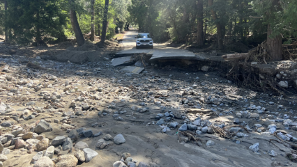 A car parked in front of a washed out road in Seven Oaks.