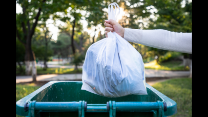 An arm drops a bag of trash into a trash receptacle. It's a blue receptacle.