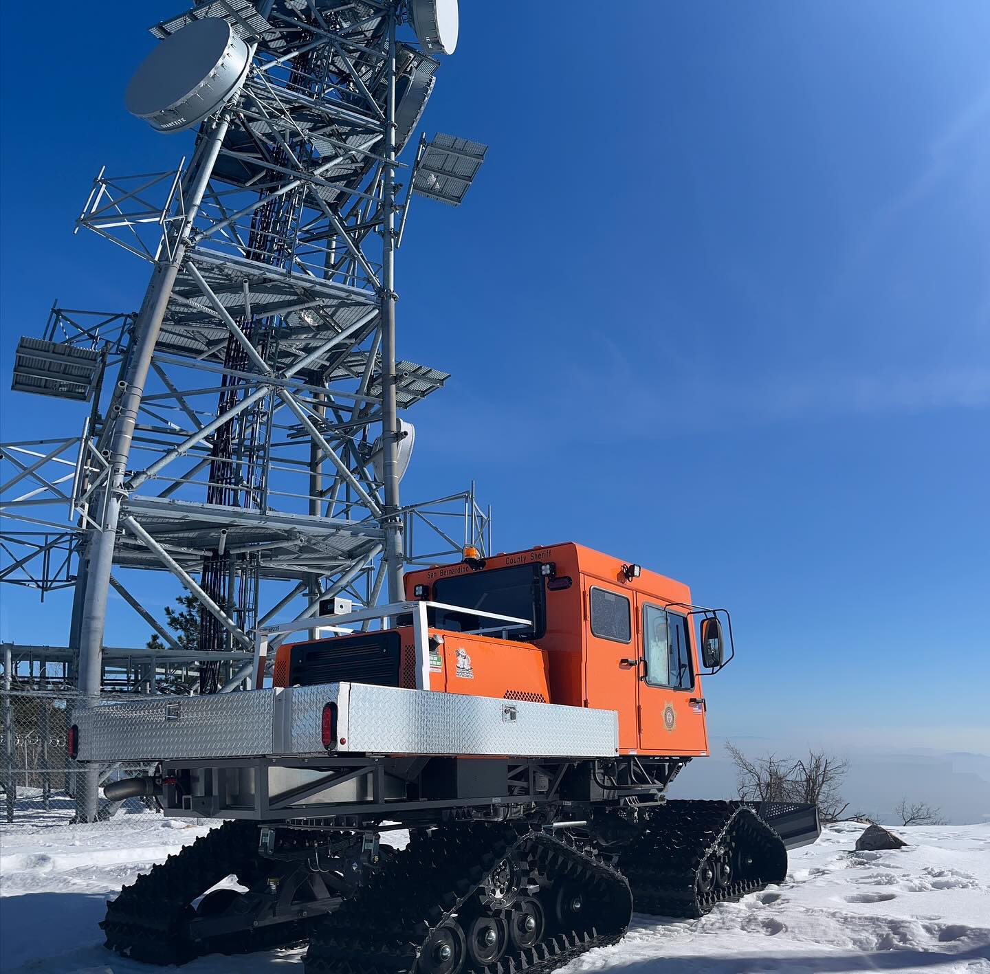 A new Sno-Cat parked next to a communications tower with snow on the ground.