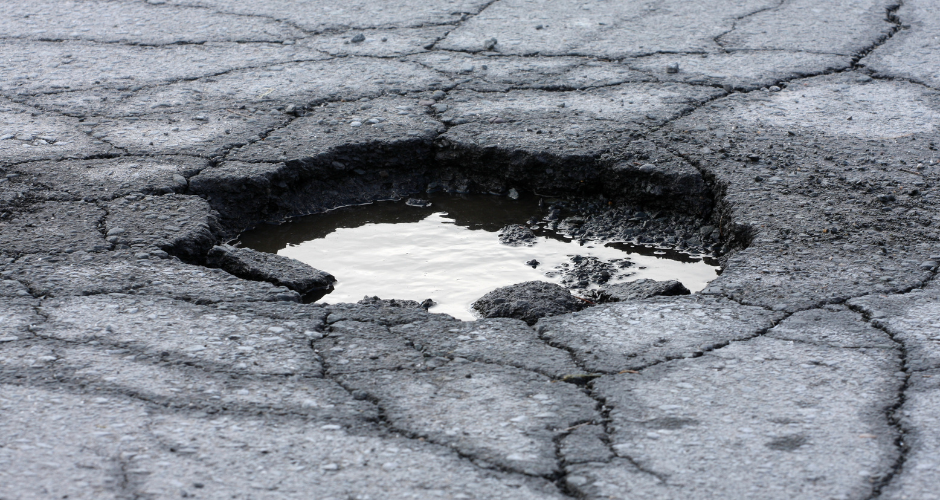 A pothole in a street. The pothole contains water.