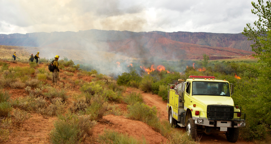 Firefighters watch a prescribed burn. A fire engine sits in the foreground.