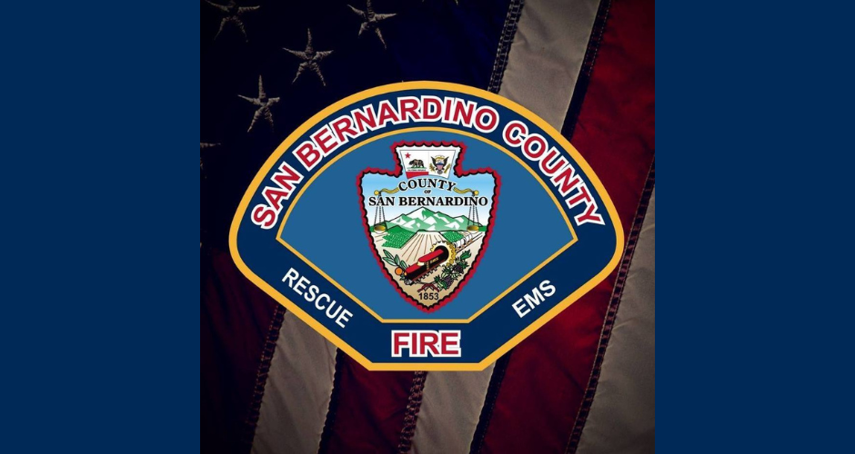 The San Bernardino County Fire Department logo sits atop an American flag. The logo says, "San Bernardino County Fire; Rescue, EMS." There is a blue background on either side of the flag.