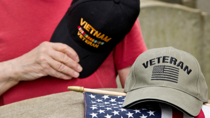 Hand holding a Vietname Veteran hat, another Veteran hat, and an American flag