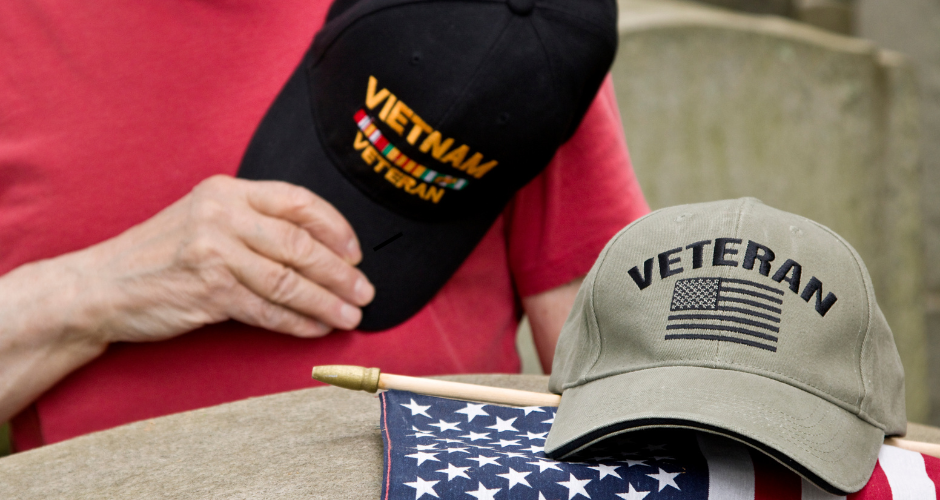 Hand holding a Vietname Veteran hat, another Veteran hat, and an American flag