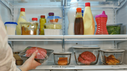 A hand reaches into a refrigerator full of food.