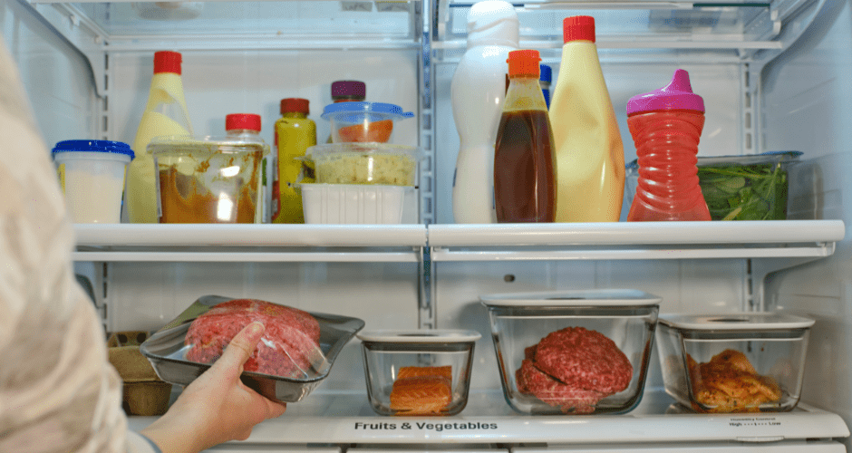 A hand reaches into a refrigerator full of food.