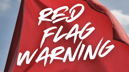 A red flag blowing in the wind with the words RED FLAG WARNING