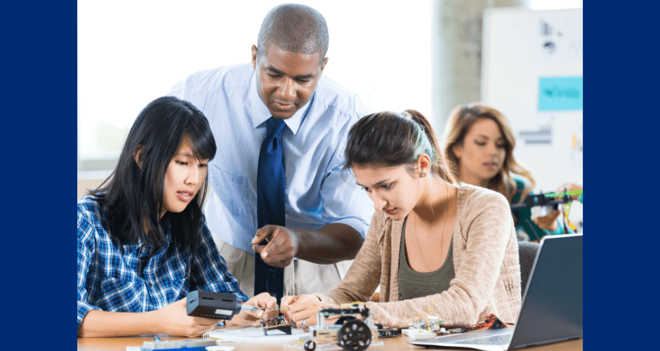 A group of high school students receive direction from their teacher in a STEM classroom.