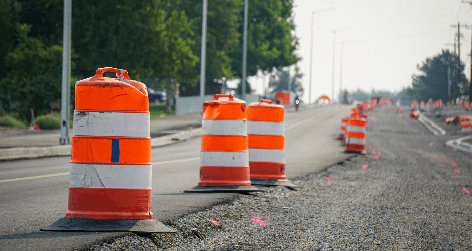 Orange and white traffic warning barrels are placed alongside roadwork that is underway on a local street.