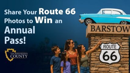 A woman and three children look at the Barstow Route 66 pedestal statue. One of the youngsters is pointing at it. Text on the image says SHARE YOUR ROUTE 66 PHOTOS TO WIN AN ANNUAL PASS! there's also a county logo on there.