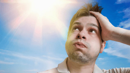 A handsome young man in a white shirt reacts to the heat generated by a blazing sun overhead.