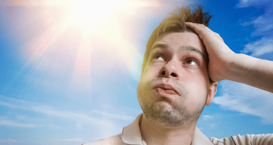 A handsome young man in a white shirt reacts to the heat generated by a blazing sun overhead.