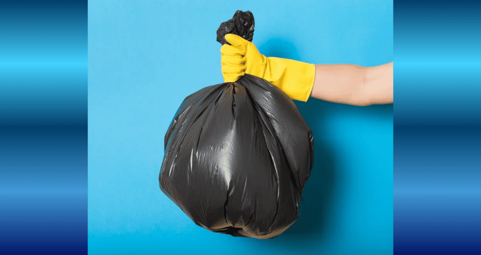 A single black trash bag is held by a yellow gloved hand against a light blue background.